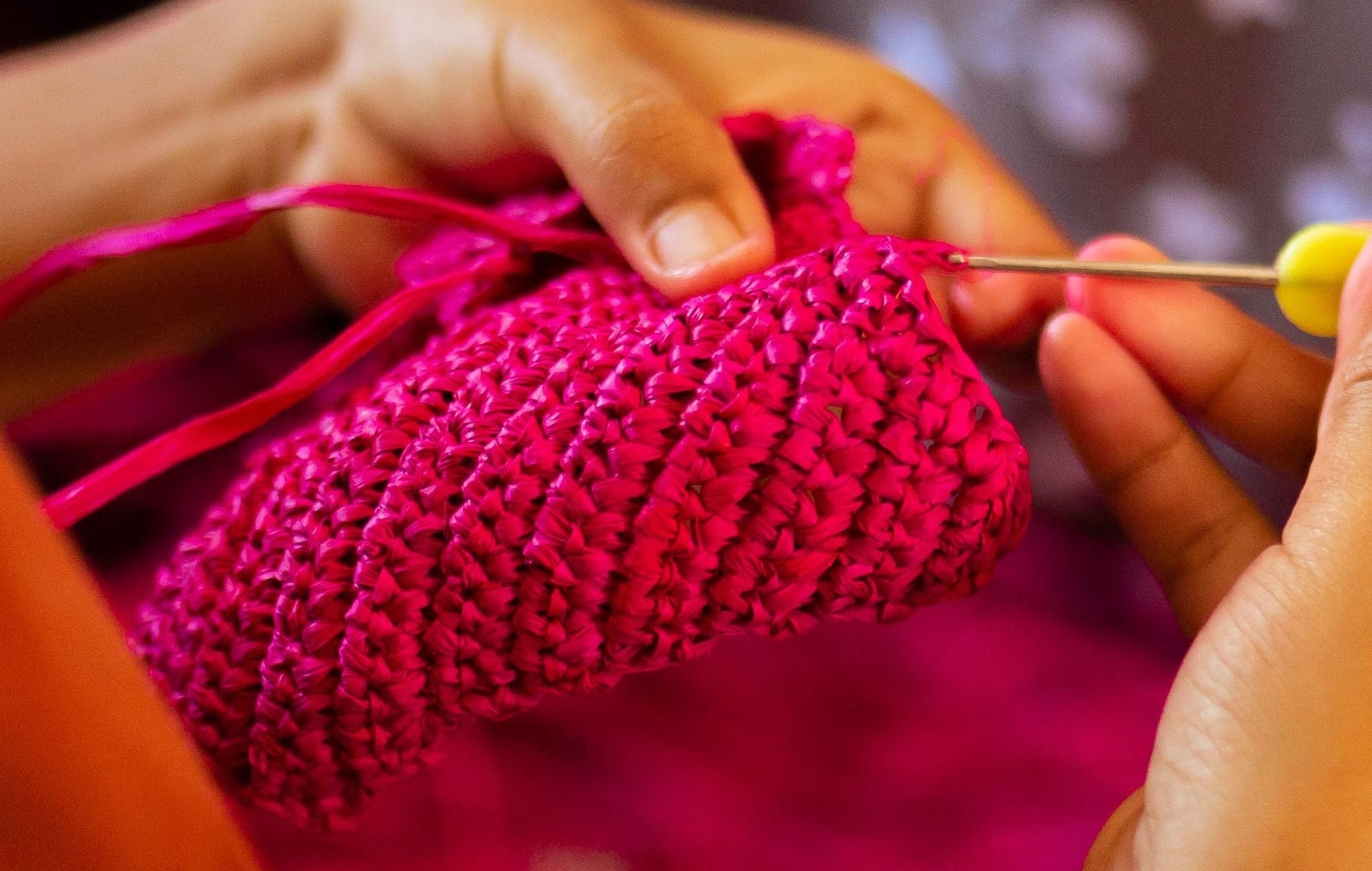 Close-up of hands knitting a pink fabric with a blurred background